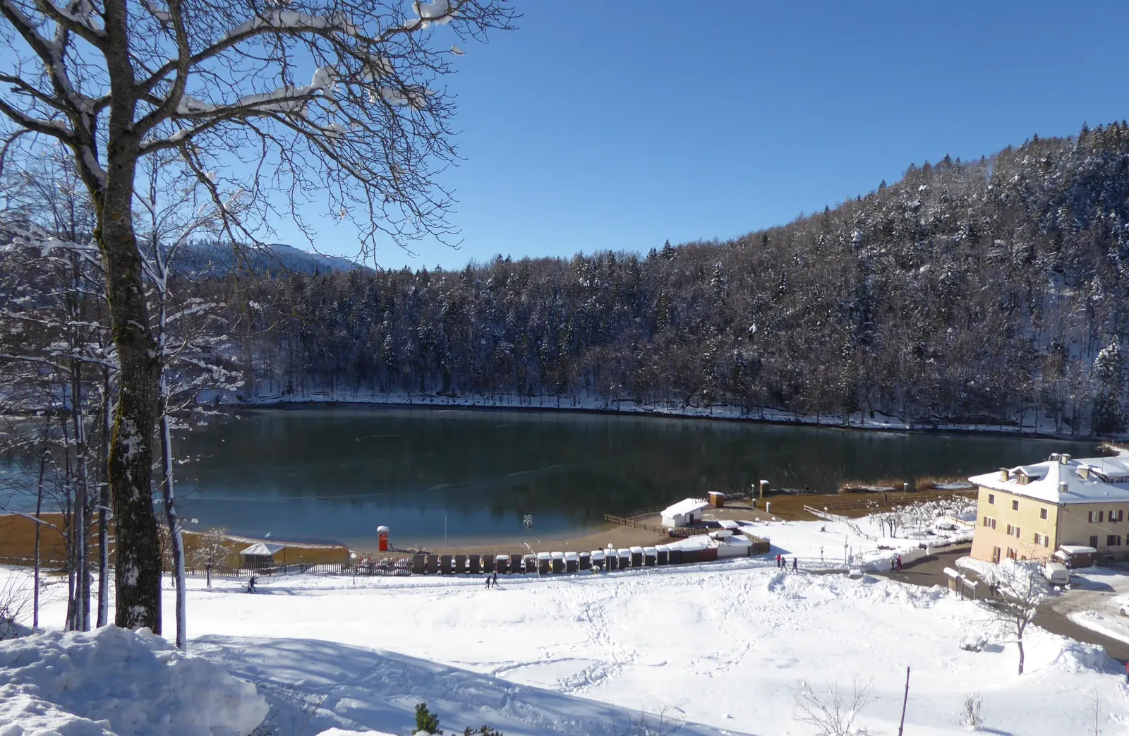 Lago di Lavarone coperto di neve in una giornata di sole, boschi imbiancati tutto intorno