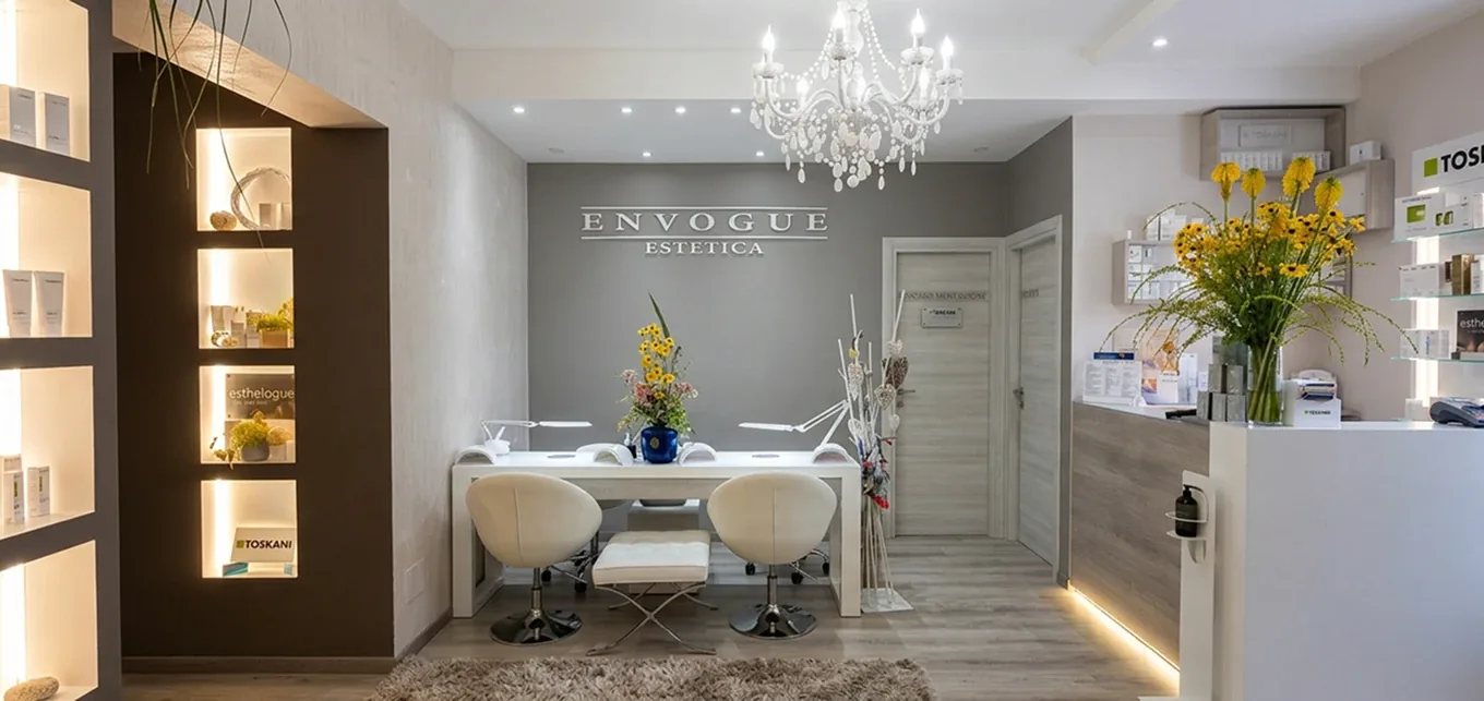 La reception di Envogue con l’insegna, il lampadario, le mensole illuminate con i prodotti Toskani ed Esthelogue e i fiori gialli