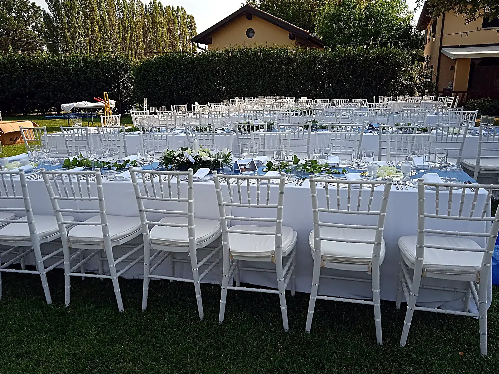 Allestimento di un evento con sedie bianche e un lungo tavolo decorato con fiori