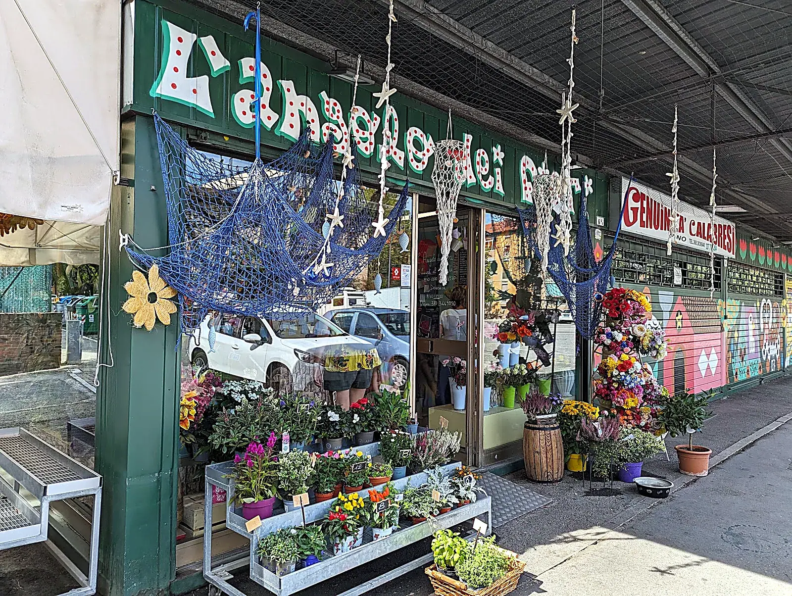Esterno del negozio con tenda verde, piante e fiori sul marciapiede